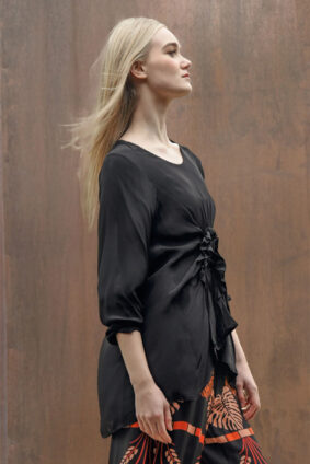Model wearing the World of Wonders top tucked into tailored trousers, highlighting the flowing silhouette and ruched texture.