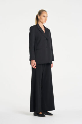 Model wearing Mela Purdie Suit Pant in Black with a matching black tailored blazer.