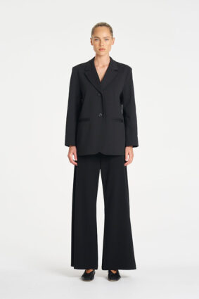 Model wearing Mela Purdie Suit Pant in Black with a matching black tailored blazer.