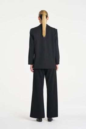 Model wearing Mela Purdie Suit Pant in Black with a matching black tailored blazer.