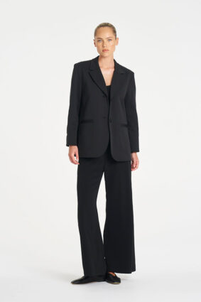 Model wearing Mela Purdie Suit Pant in Black with a matching black tailored blazer.