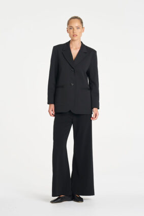 Model wearing Mela Purdie Suit Pant in Black with a matching black tailored blazer.