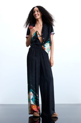 Desigual Tropical Pant Negro front view showing relaxed resort-inspired silhouette and vibrant tropical print of oversized florals and lush palm leaves