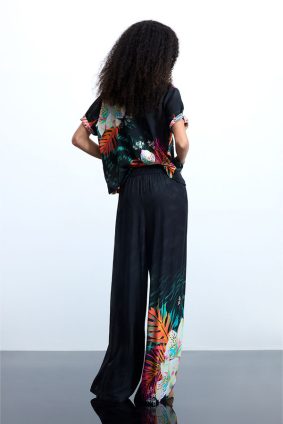 Desigual Tropical Pant Negro front view showing relaxed resort-inspired silhouette and vibrant tropical print of oversized florals and lush palm leaves