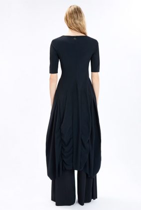 Model wearing the High Tech On Top Dress, featuring a fitted bodice, gathered seams, a wide silhouette from the waist down, and an asymmetric hem.