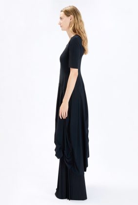 Model wearing the High Tech On Top Dress, featuring a fitted bodice, gathered seams, a wide silhouette from the waist down, and an asymmetric hem.