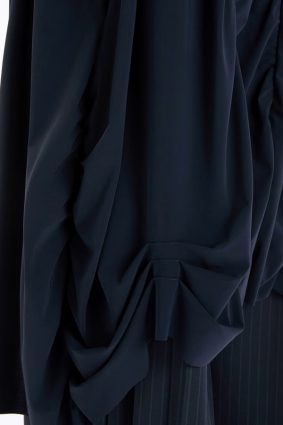 Model wearing the High Tech On Top Dress, featuring a fitted bodice, gathered seams, a wide silhouette from the waist down, and an asymmetric hem.