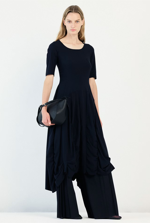 Model wearing the High Tech On Top Dress, featuring a fitted bodice, gathered seams, a wide silhouette from the waist down, and an asymmetric hem.