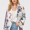 Model wearing the Johnny Was Noemi Jacket Armeria White, an ivory cotton statement jacket featuring rich floral embroidery, paisley motifs, and intricate geometric contrast detailing in cobalt, crimson, and turquoise.
