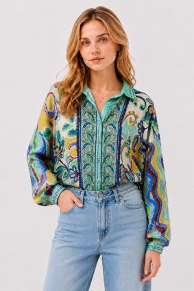 Model wearing the Johnny Was The Audrey Button Up Shirt Rosea, a fluid silk blouse featuring an intricate medley of paisley, floral, and ornamental motifs in aqua, turquoise, cobalt, lime, and golden yellow.