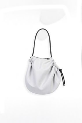 The In.Zu Cocconeo Bag Off White Latex Owl features a soft, rounded silhouette with elegant gathered detailing, adjustable black drawstrings and a sleek shoulder strap.