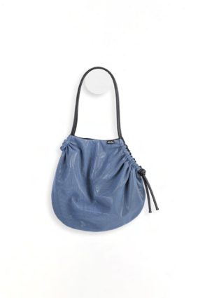 The In.Zu Cocconeo Bag Riverside Over Film features a relaxed crescent silhouette in a rich blue shade, with a textured dot finish and adjustable black shoulder strap.